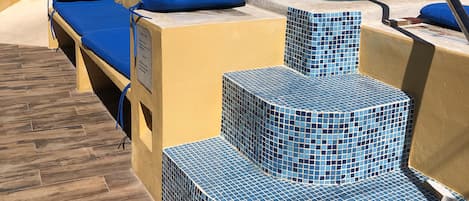 A pool area with blue-tiled steps, lounge chairs, and a wooden deck.
