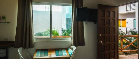 A room with a window, a table with chairs, a television mounted on the wall, and a door leading to an outdoor area.