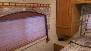 A compact bedroom with a wooden headboard, a wooden wardrobe, and a patterned bedspread. - RV Space at Balloon Fiesta Park VIP North Lot (RV Available also) (Albuquerque)