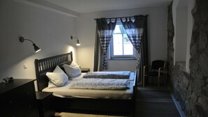 Een slaapkamer met een bed, nachtkastjes, een lamp, een stoel en een raam met gordijnen.