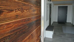 Een houten muur met een zichtbare scheur, een witte bank en een grijze betegelde vloer in een gang.