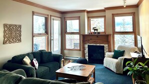 A cozy living room with a fireplace, large windows, and a comfortable seating area. - Rare Top 3rd Floor Corner Grandview Condo with Elevator & Extra Large Balcony (Silver Star Mountain)