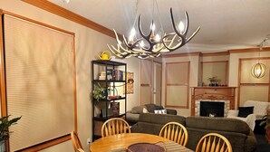 A cozy living room with a fireplace, a dining table with chairs, a bookshelf, and a large chandelier. - Rare Top 3rd Floor Corner Grandview Condo with Elevator & Extra Large Balcony (Silver Star Mountain)