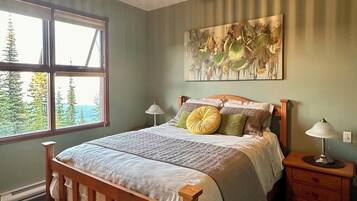 A bedroom with a wooden bed, a ceiling fan, a window with a view of trees, and a painting on the wall.