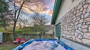 Un jacuzzi en un patio trasero con un muro de piedra, dos sillas Adirondack rojas y una valla de madera.