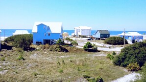 A coastal area with several buildings, including a prominent blue house with a white roof, surrounded by grassy terrain and a clear view of the ocean. - HEATED PRIVATE POOL, 5 bedrooms, Oceanview, Newly decorated and furnished (Gulf Shores)