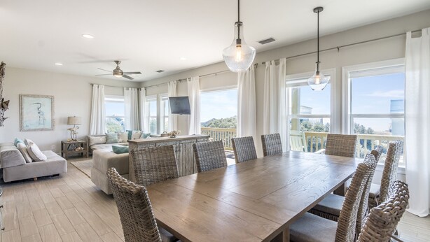 A spacious dining area with a large wooden table and wicker chairs, a sofa, and a TV on the wall. - HEATED PRIVATE POOL, 5 bedrooms, Oceanview, Newly decorated and furnished (Gulf Shores)