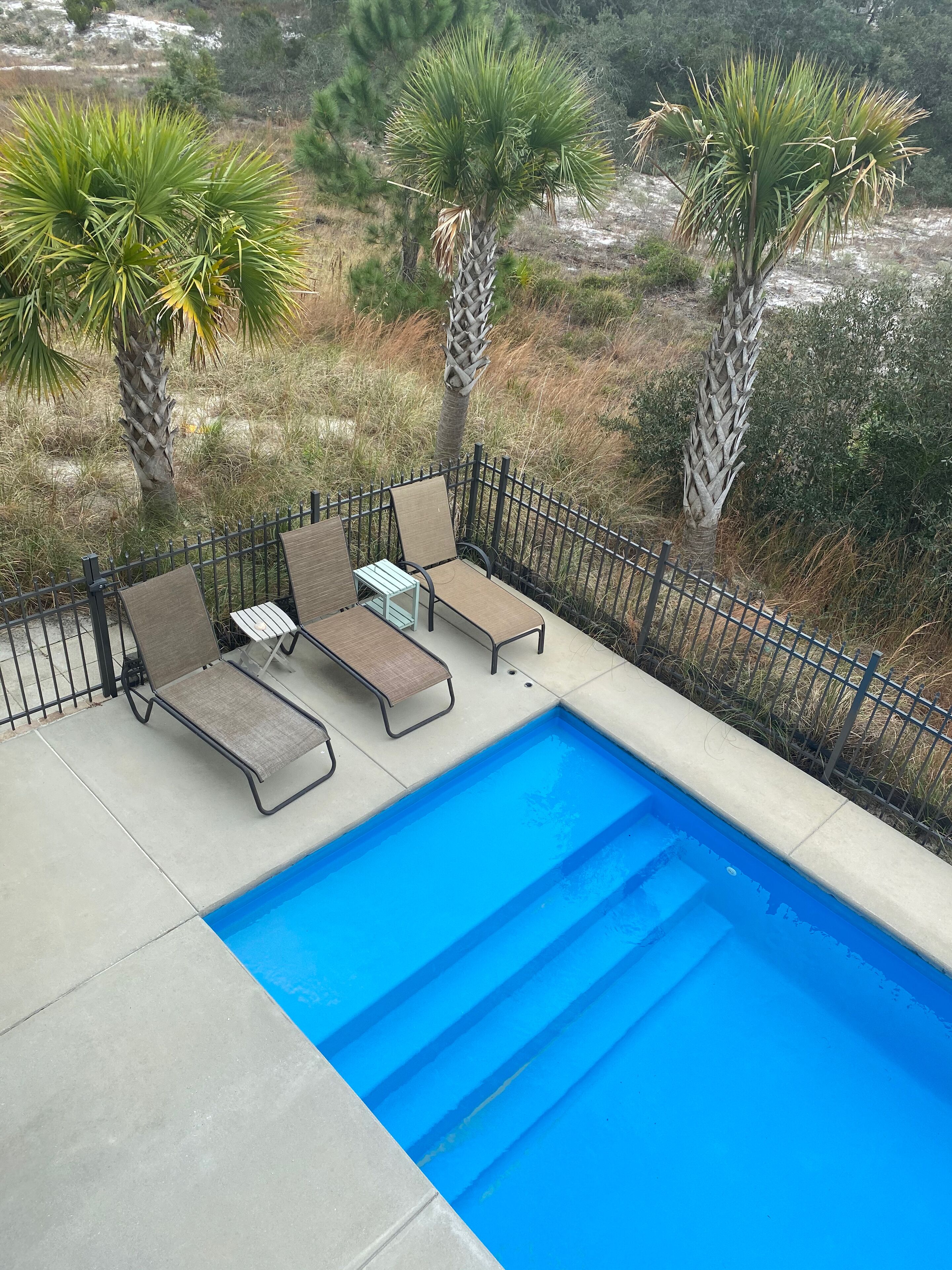 A poolside area with three lounge chairs and a small table, surrounded by a black metal fence.