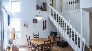 A spacious living area with a wooden dining table, chairs, a TV, and a staircase with white railings. - Spring Meadows | Spend Spring in Flagstaff! (Flagstaff)