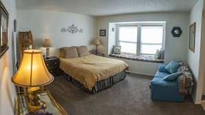 A bedroom with a bed, a blue sofa, a window with a view, a lamp, and a decorative wall piece. - Spring Meadows | Spend Spring in Flagstaff! (Flagstaff)