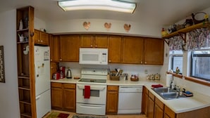 A compact kitchen with wooden cabinets, a white refrigerator, a microwave, a stove, and a dishwasher. - Spring Meadows | Spend Spring in Flagstaff! (Flagstaff)