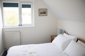 A bedroom with a bed, a window, a radiator, a bedside table with a lamp, and a framed picture on the wall.