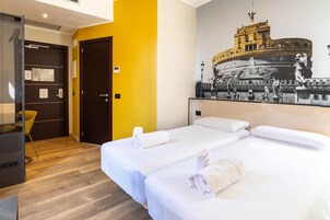 Habitación de hotel con dos camas, un cabecero amarillo, un gran mural en blanco y negro de un edificio histórico y suelo de madera.
