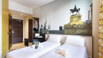 Habitación de hotel con dos camas, un armario, un escritorio con computadora y un mural grande de un monumento histórico.