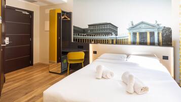 A hotel room with a bed, a desk, a chair, and a large mural of a building.