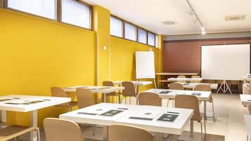 Una sala conferenze con tavoli bianchi, sedie beige e una lavagna grande.