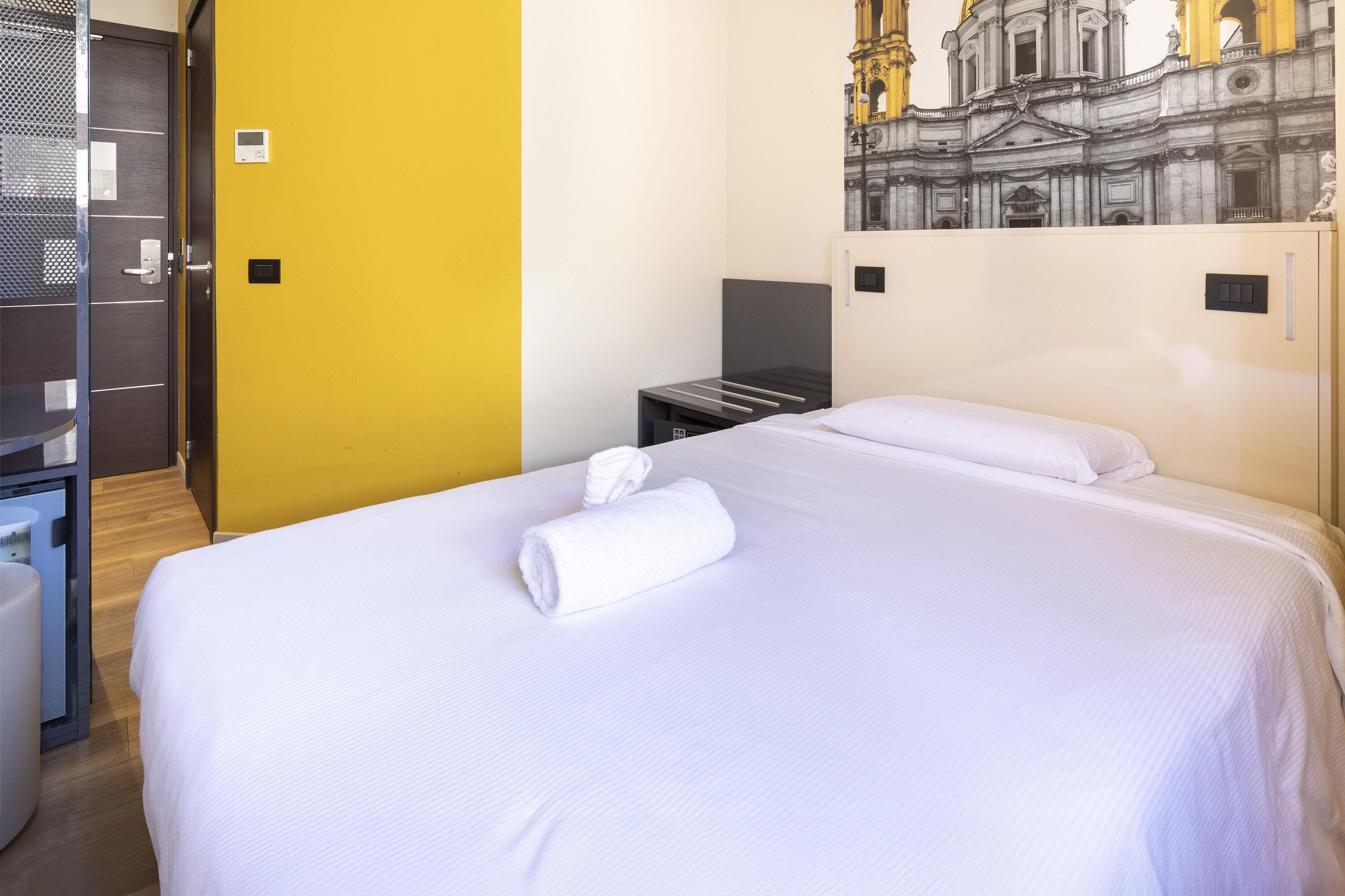 A hotel room with a bed, a nightstand, a small table, a chair, and a door.
