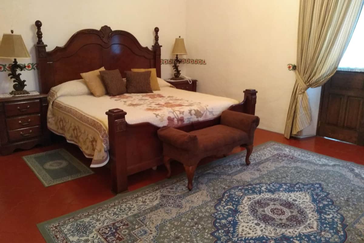 Ein traditionell eingerichtetes Schlafzimmer mit einem hölzernen Bett, zwei Nachttischen, einem Sessel und einem gemusterten Teppich.