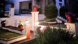 Un bâtiment blanc doté de fenêtres en arc de cercle et d’une entrée centrale, entouré de jardins bien entretenus et de plantes en pot.