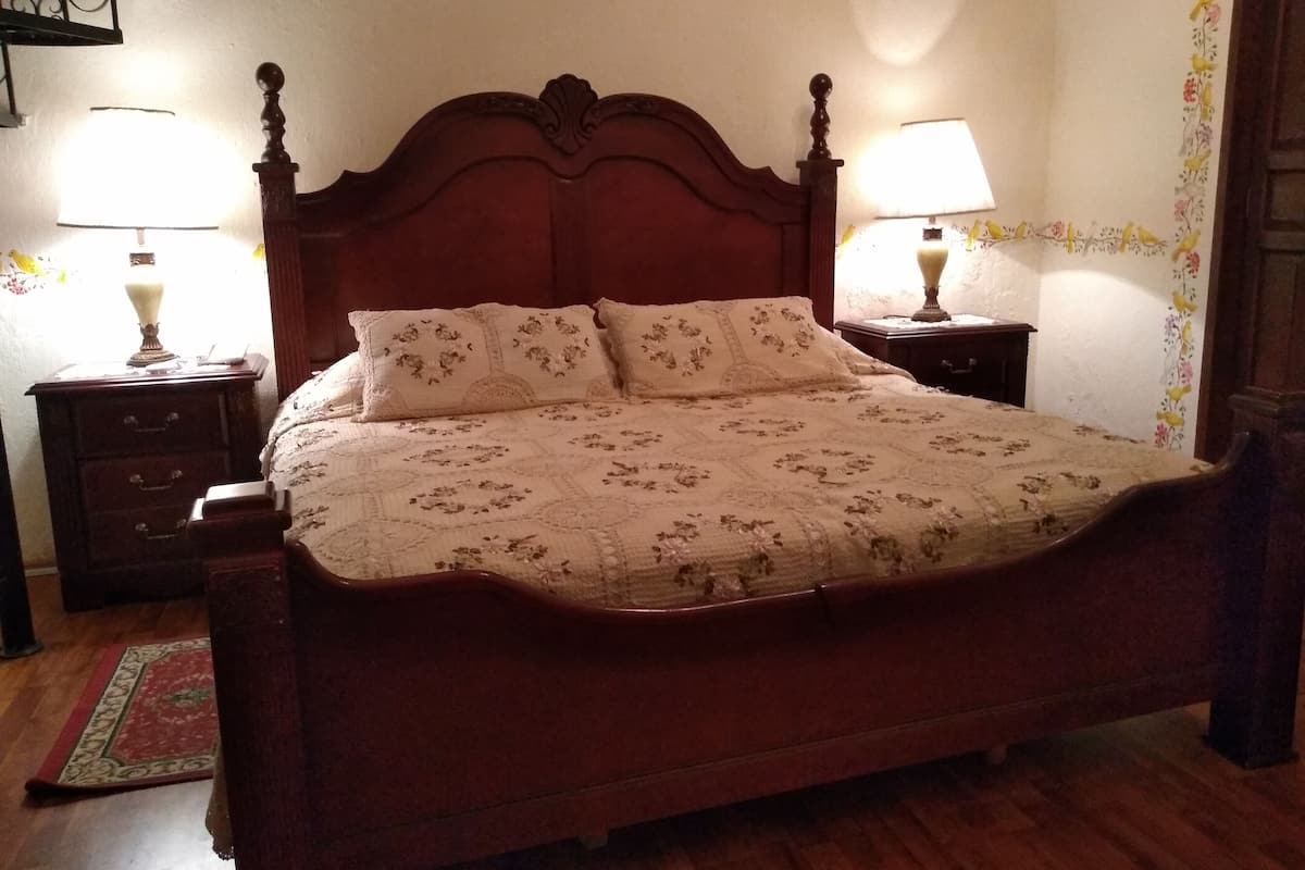 Ein hölzernes Bett mit floralem Bettbezug und passenden Kissen, beides von Nachttischen mit Lampen eingerahmt.