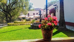 Une cour avec une fontaine, un pot de fleurs, et un bâtiment surmonté d’un auvent rouge.