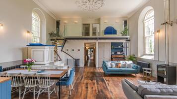 A spacious living area with a wooden floor, a dining table with chairs, a blue sofa, and a fireplace.