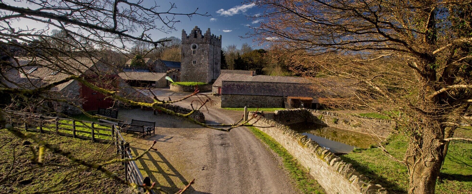 Un paysage rural avec un bâtiment en pierre, une construction à toit de chaume et un petit étang.