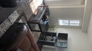A living room with a brown leather sofa, a glass coffee table, a TV, and a window with a view of buildings. - Premium Elite suites (Oshawa)