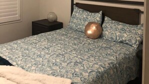 A bedroom with a bed, two wall-mounted paintings, a nightstand, and a window with blinds. - Premium Elite suites (Oshawa)