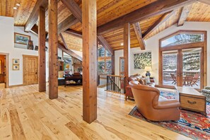 A spacious living area with wooden beams, a fireplace, and a view of the outdoors. - Cascade Village Private Mountain Home (Vail)