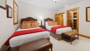 Una camera d'albergo con due letti, una panca, un comodino, una lampada e una porta che dà su un armadio.