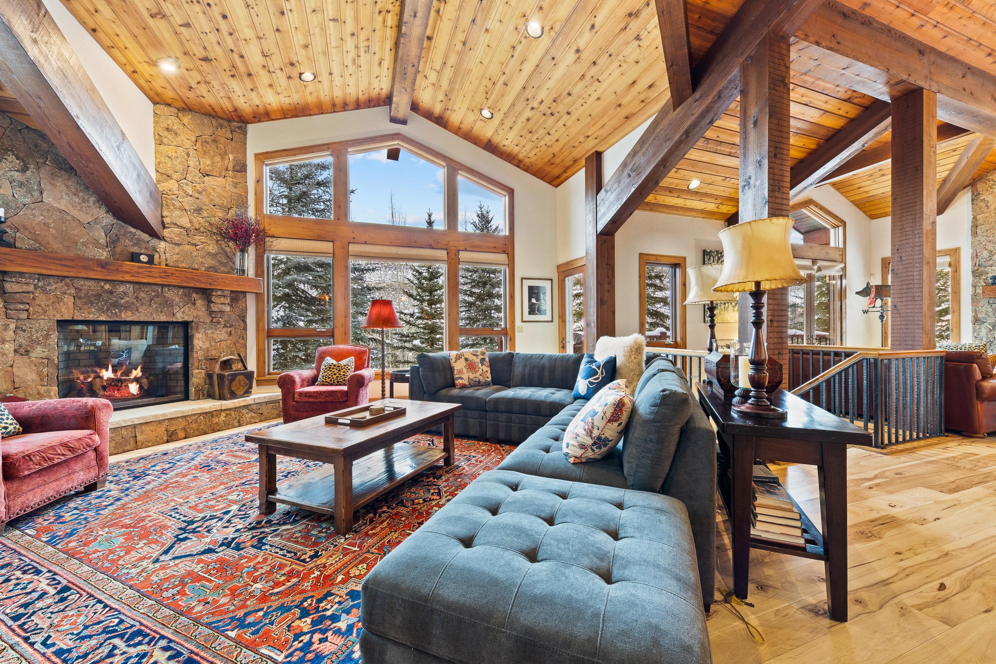 A spacious living room with a fireplace, large windows, and a high wooden ceiling.