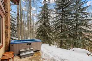 A hot tub outside a stone building with a snowy forest background.