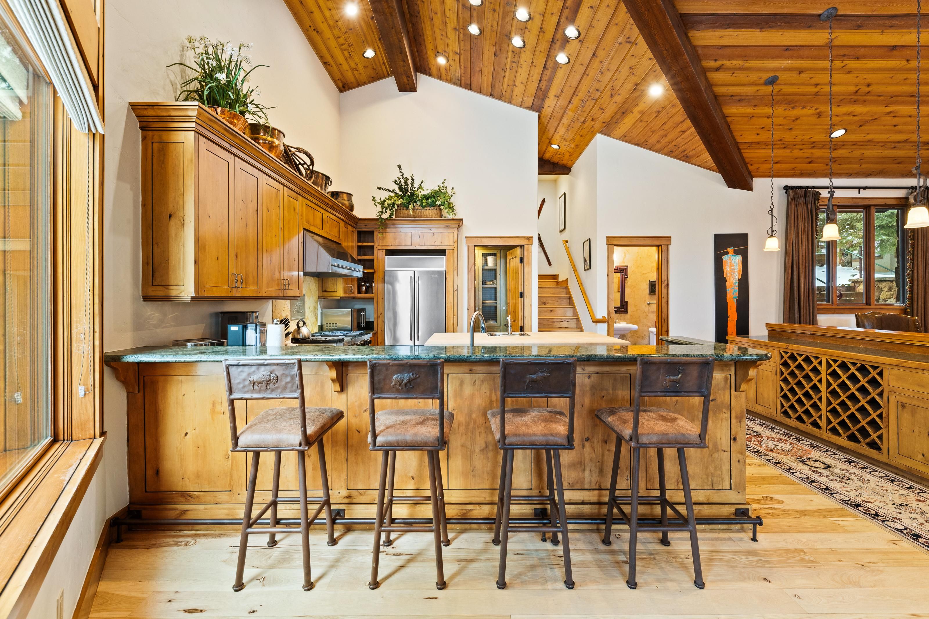 A spacious kitchen with wooden cabinets, a stainless steel refrigerator, and a bar area with stools.