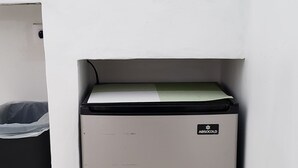 Une petite cuisine équipée comprenant un four grille-pain rouge, un petit réfrigérateur et une machine à café, le tout posé sur un plan de travail blanc.