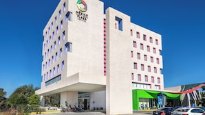 Un hotel moderno con un logotipo destacado, varios pisos y una zona de entrada verde.