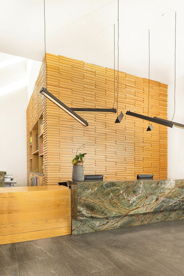 Una zona de recepción con pared de madera, mostrador de mármol y planta en maceta.
