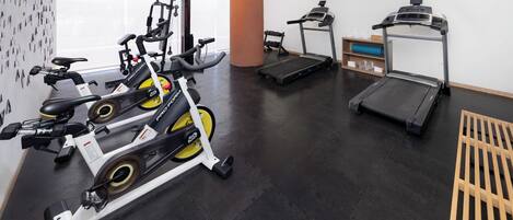 Een sportschool met cardioapparatuur, een loopband en een hometrainer.