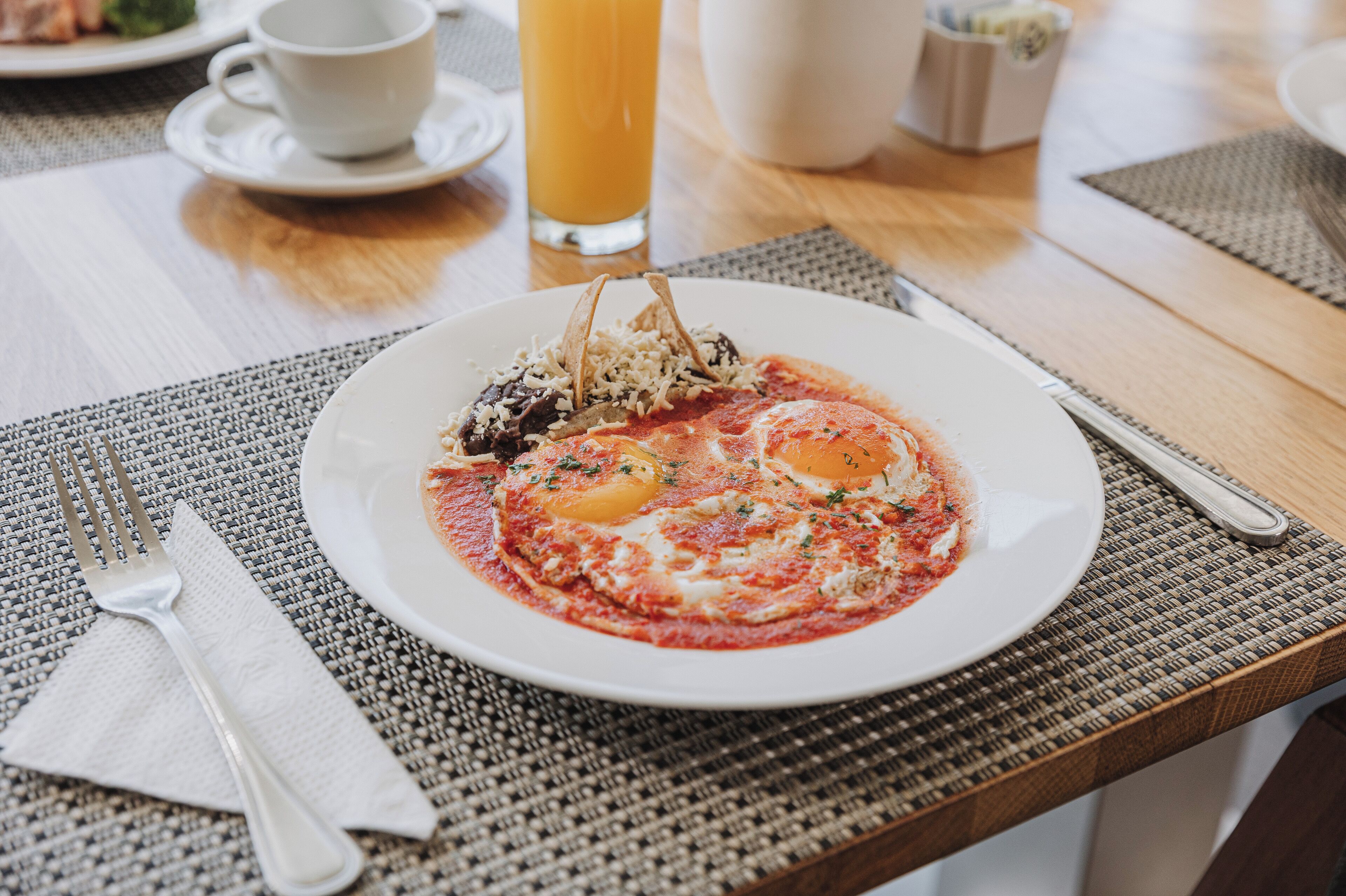 Ein Frühstückstisch mit Speisen, Orangensaft und Besteck.