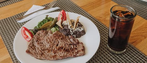 Un plato de comida con un filete, verduras y un vaso de bebida helada sobre una mesa.