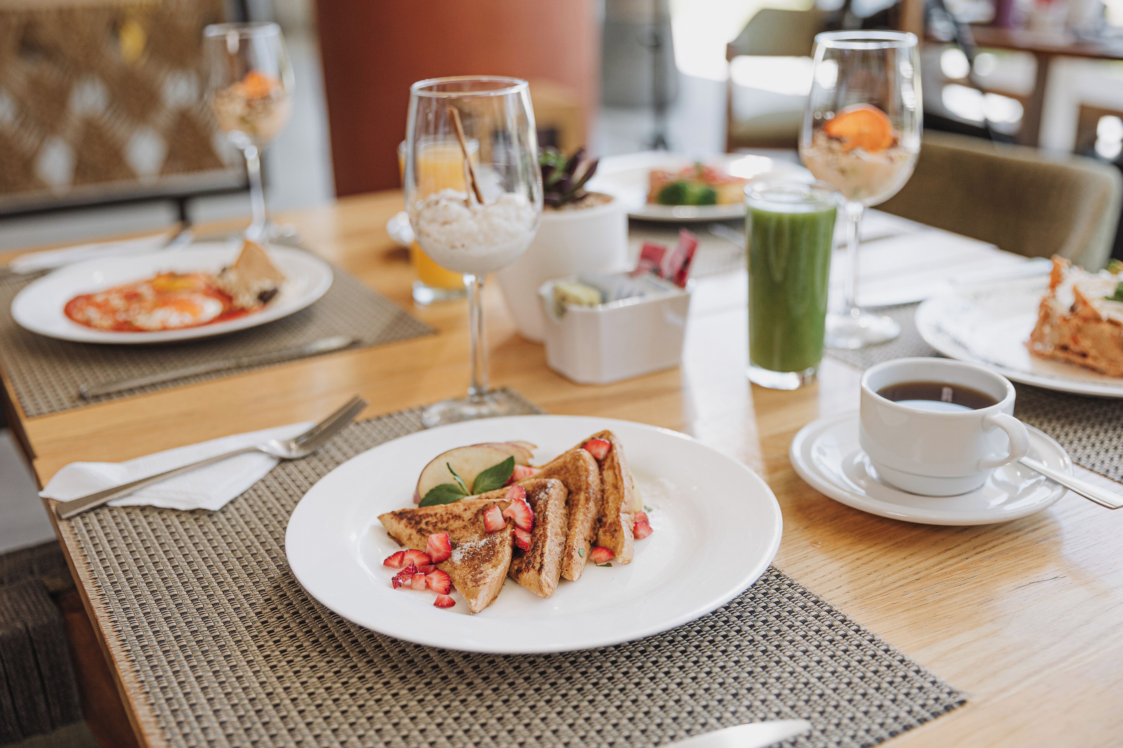 A dining table with breakfast items including toast with strawberries, a glass of orange juice, and a green smoothie.