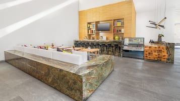 Una moderna zona de recepción con un mostrador de mármol, un área de descanso con un sofá blanco, una pared de madera con estanterías, un televisor y una máquina expendedora.