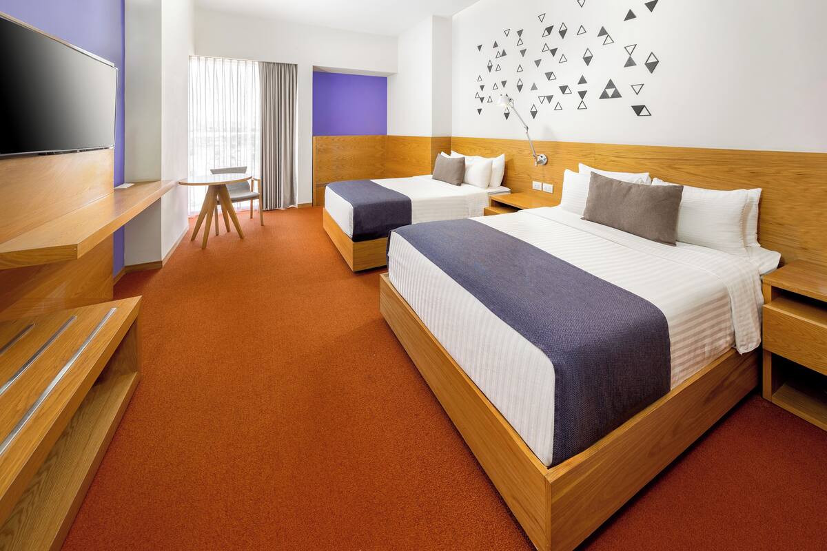 Ein Hotelzimmer mit zwei Betten, einem Fernseher, einem Schreibtisch und einem Stuhl.