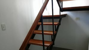 A wooden staircase with black metal railings in a room with white walls and a tiled floor. - Apart No Me Olvides (Federacion)