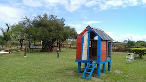 A colorful playhouse with a ladder, surrounded by a grassy yard and trees. - Apart No Me Olvides (Federacion)
