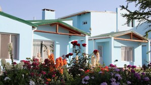 A light blue building with a green roof, surrounded by colorful flowers. - Apart No Me Olvides (Federacion)