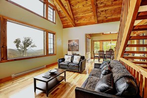 A spacious living room with a wooden ceiling, large windows, a fireplace, and a cozy seating area.