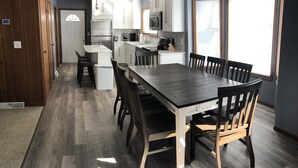 Une cuisine moderne avec des meubles blancs, un grand îlot central et un coin repas comprenant une table et des chaises en bois foncé.