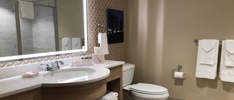A bathroom with a large mirror, a sink, a toilet, and towels hanging on the wall.