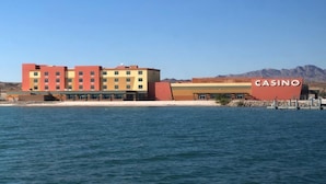 Een meerhoog gebouw met een opvallend “CASINO” bord, gelegen nabij een waterpartij met bergen op de achtergrond.